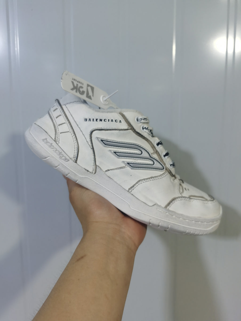 Angled view of the white Balenciaga Hampton sneaker showing the branded upper, side logo detail, heel panel, and rubber outsole.