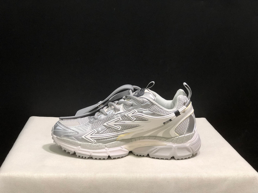 Full side profile of a white and grey sneaker showing the layered upper, directional graphics, heel structure, and chunky outsole.