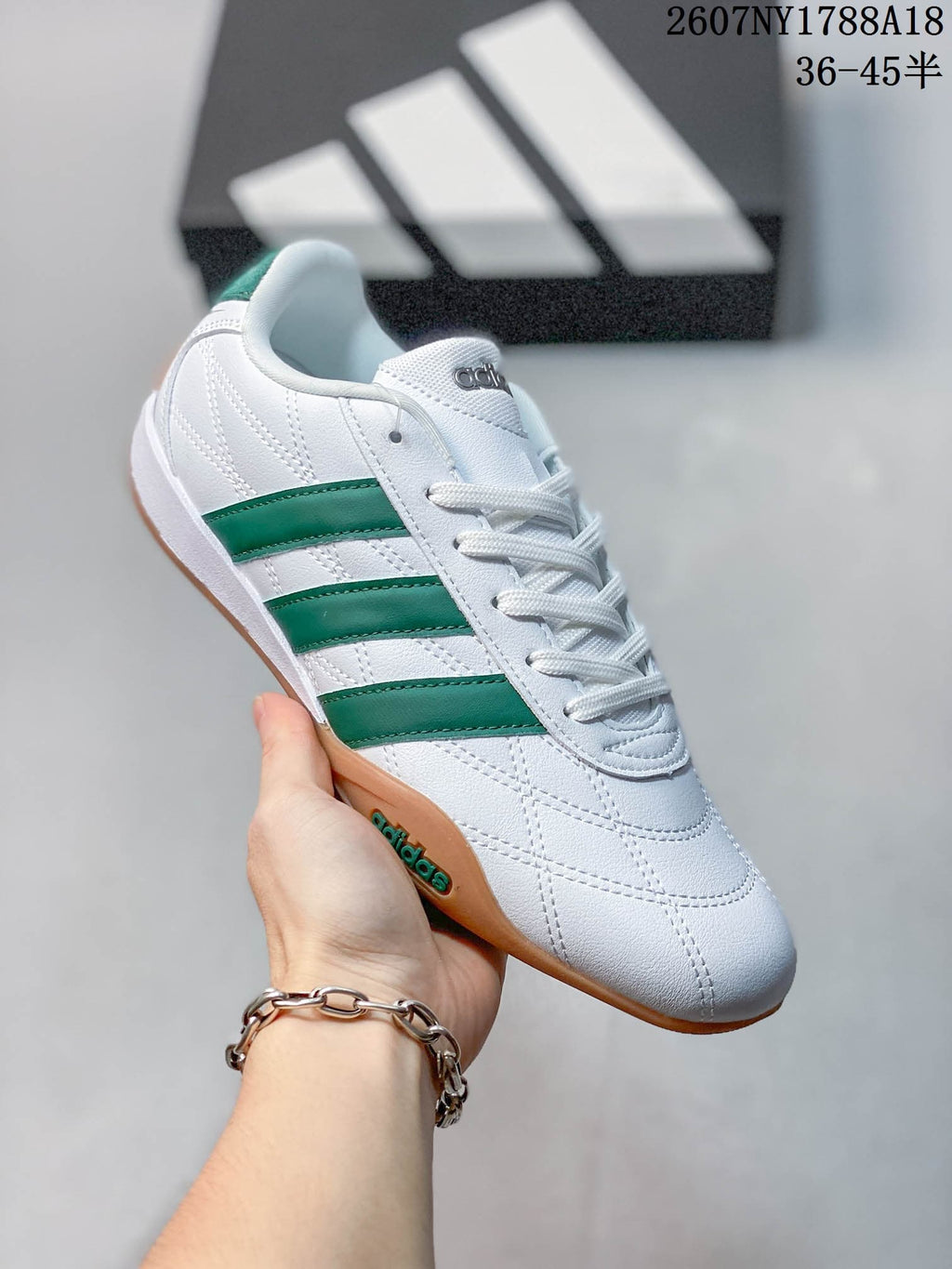 Close side view of a white adidas Adipista trainer with green stripes and a gum-colored outsole.