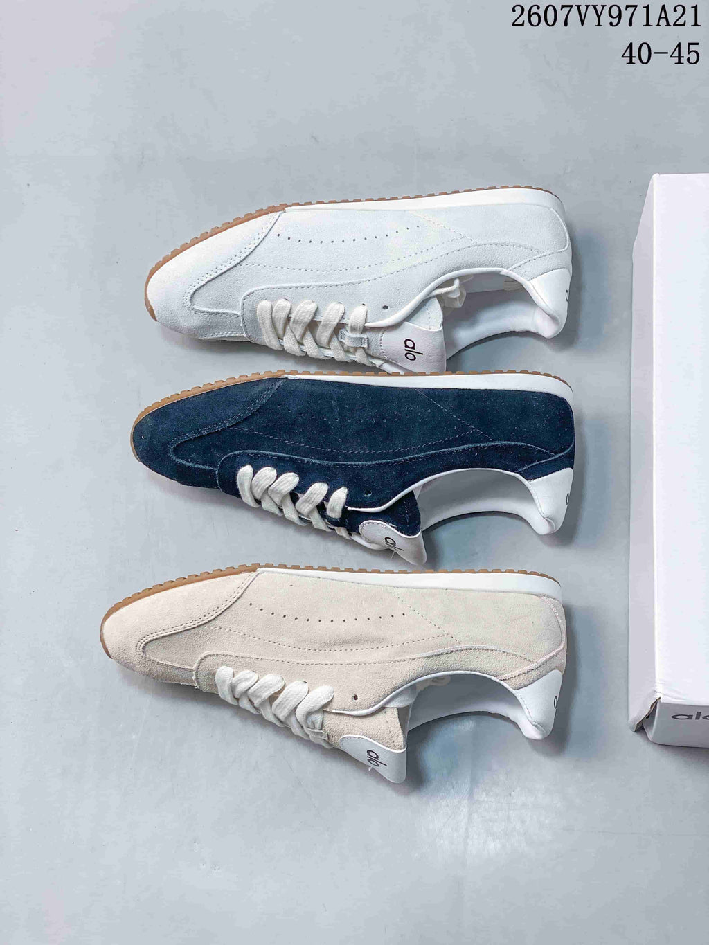 Top-down view showing white, navy, and light beige versions of the Alo Yoga low-top sneaker beside its box.