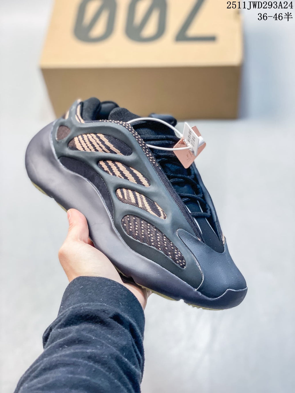 Angled side view of a black sneaker showing tan patterned panels, lace system, sculpted overlays, and attached tags.