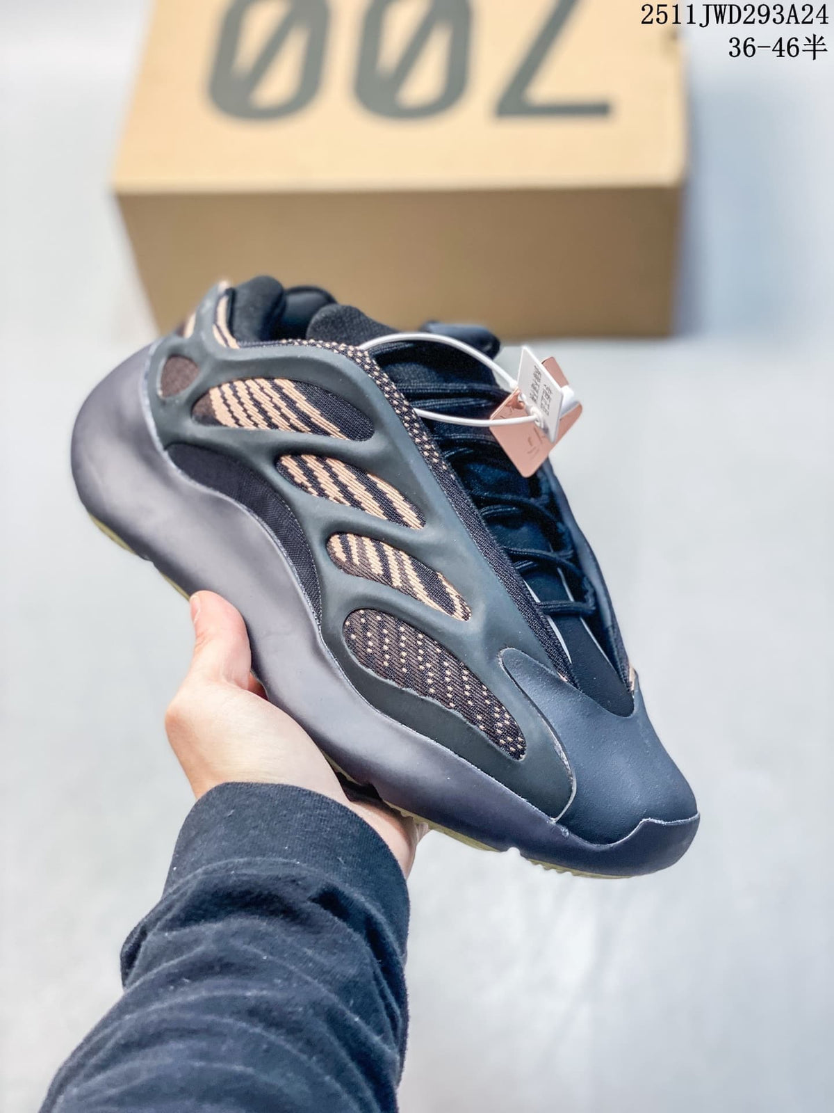 Angled side view of a black sneaker showing tan patterned panels, lace system, sculpted overlays, and attached tags.