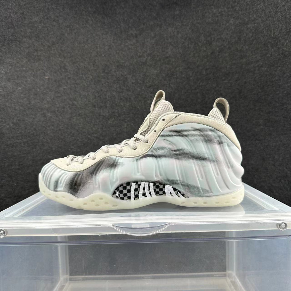 Side view of a pale high-top sneaker with dark cloudy accents and a checkerboard midfoot detail