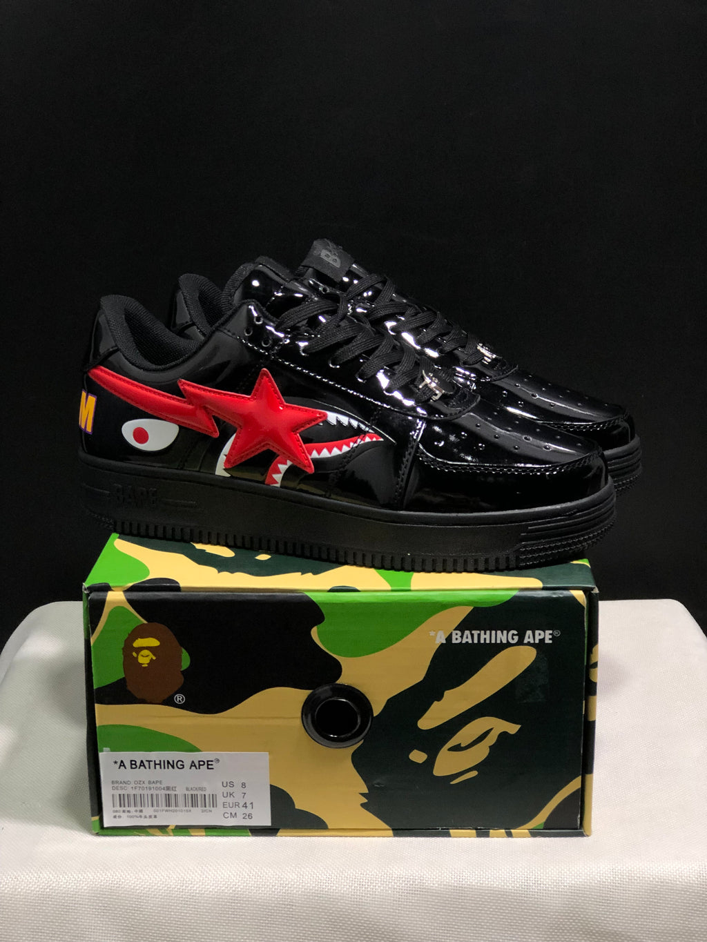 Pair of glossy black Bape Sta sneakers displayed on a camouflage BAPE shoebox; the box label shows EU 41, US 8, UK 7, and CM 26.