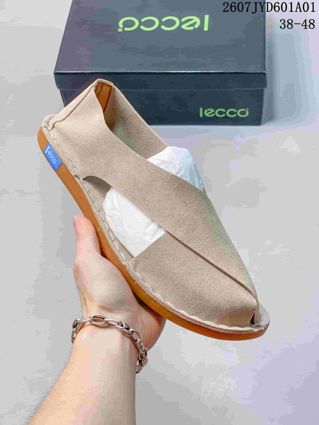 Close-up of a light beige cross-strap shoe showing its open sides and stitched sole edge; image label shows style code 2607JYD601A01 and sizes 38–48.