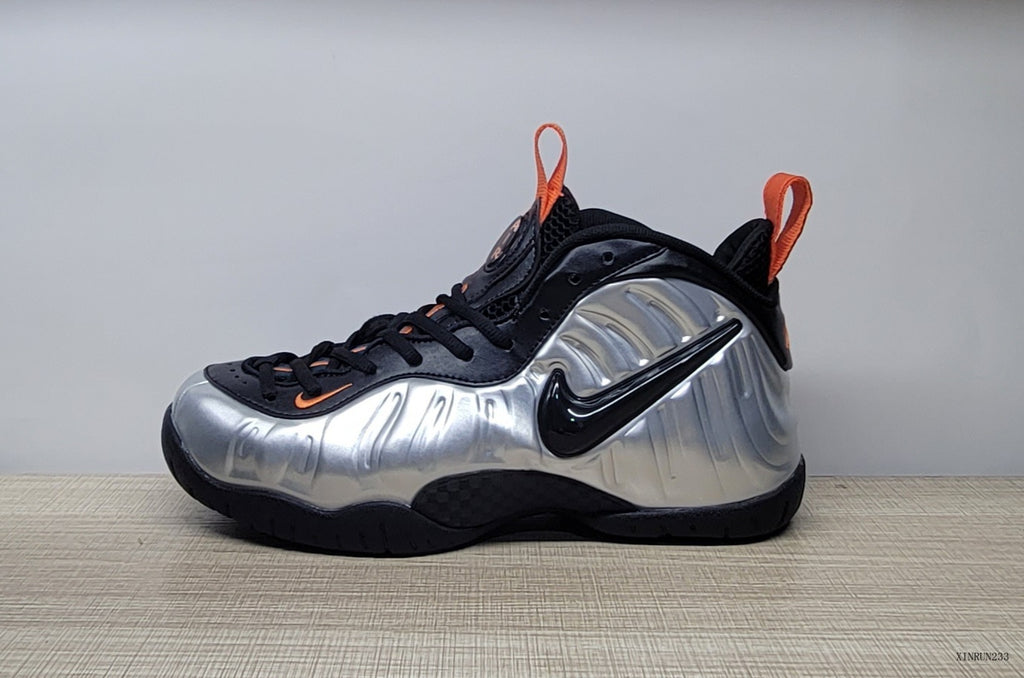 Side view of a silver and black high-top sneaker with a black Swoosh and orange accents