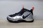 Side view of a silver and black high-top sneaker with a black Swoosh and orange accents
