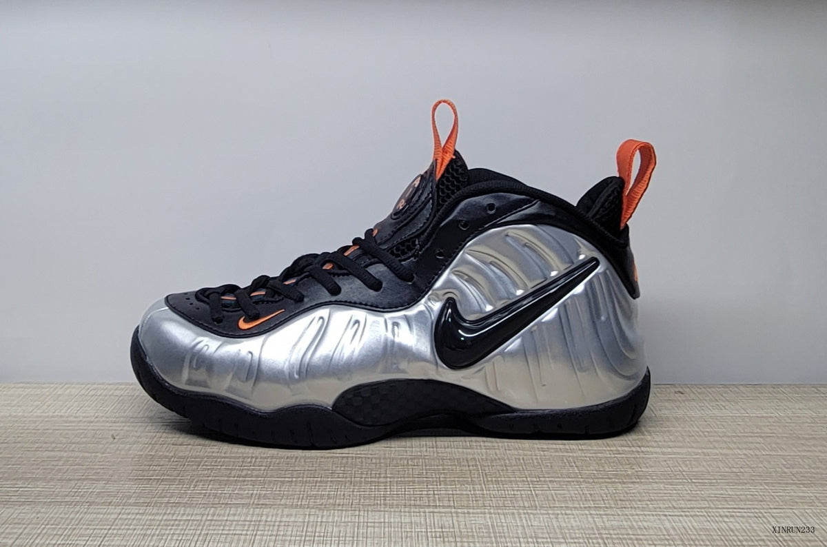 Side view of a silver and black high-top sneaker with a black Swoosh and orange accents
