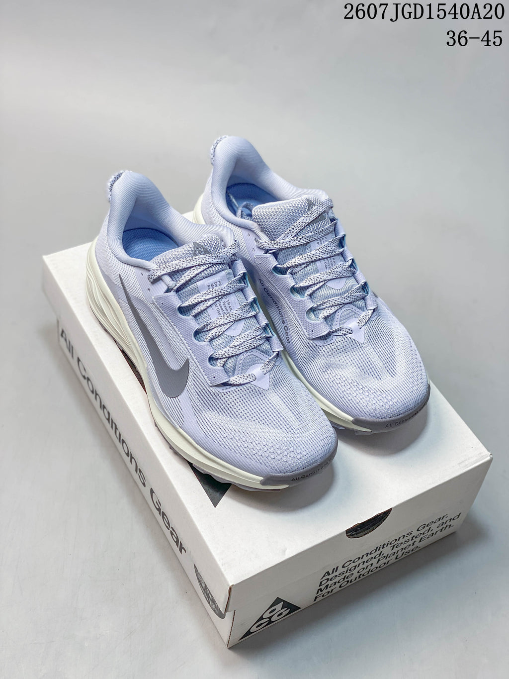 Pair of light lavender Nike ACG Pegasus Trail sneakers displayed on a shoe box, showing the woven-looking upper, laces, gray Swoosh, and cushioned midsoles.