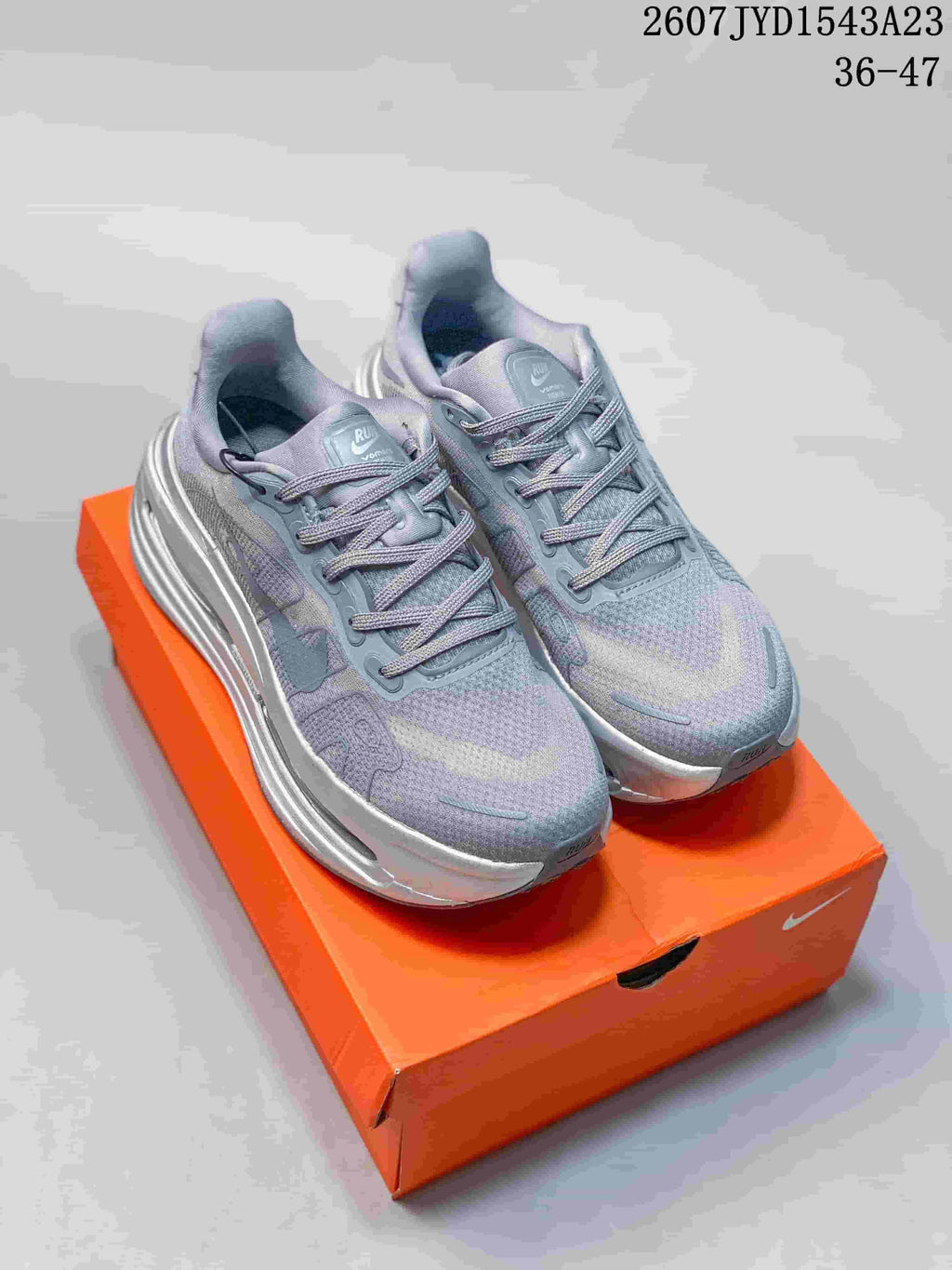 Pair of grey and soft lilac Nike Vomero Premium sneakers displayed on an orange shoebox.