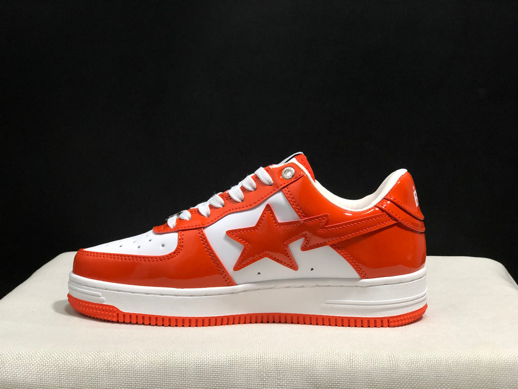 Side profile of a white and orange BAPE Sta sneaker against a dark background.