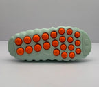Outsole view showing the light green base and multiple orange circular traction elements.