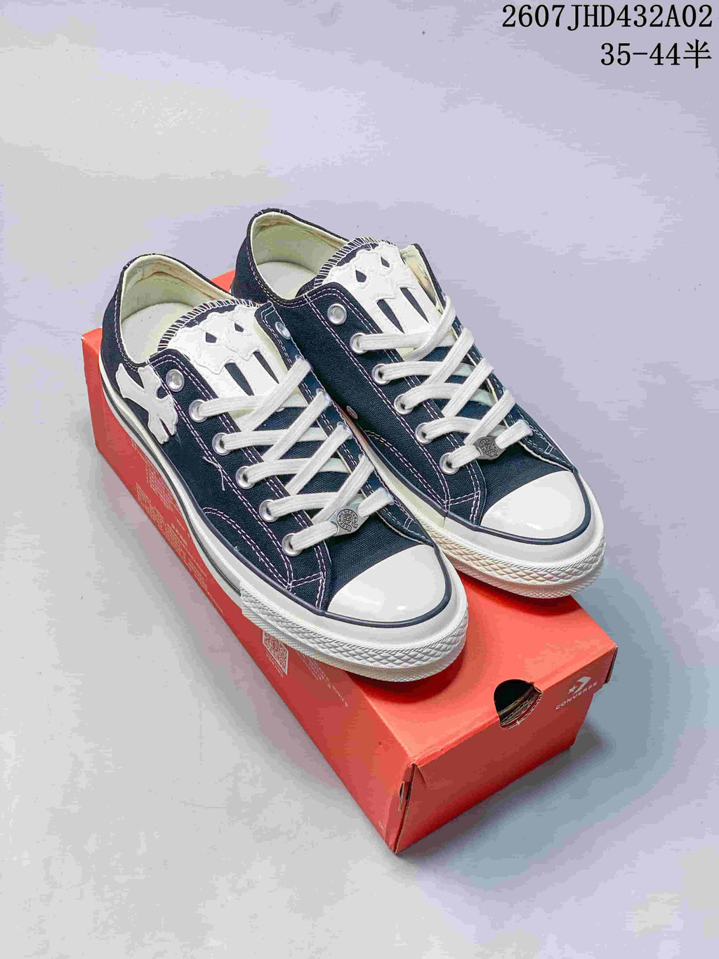 Pair of navy and white low-top Chuck Taylor-style sneakers with cross-shaped accents, shown on a red shoe box.