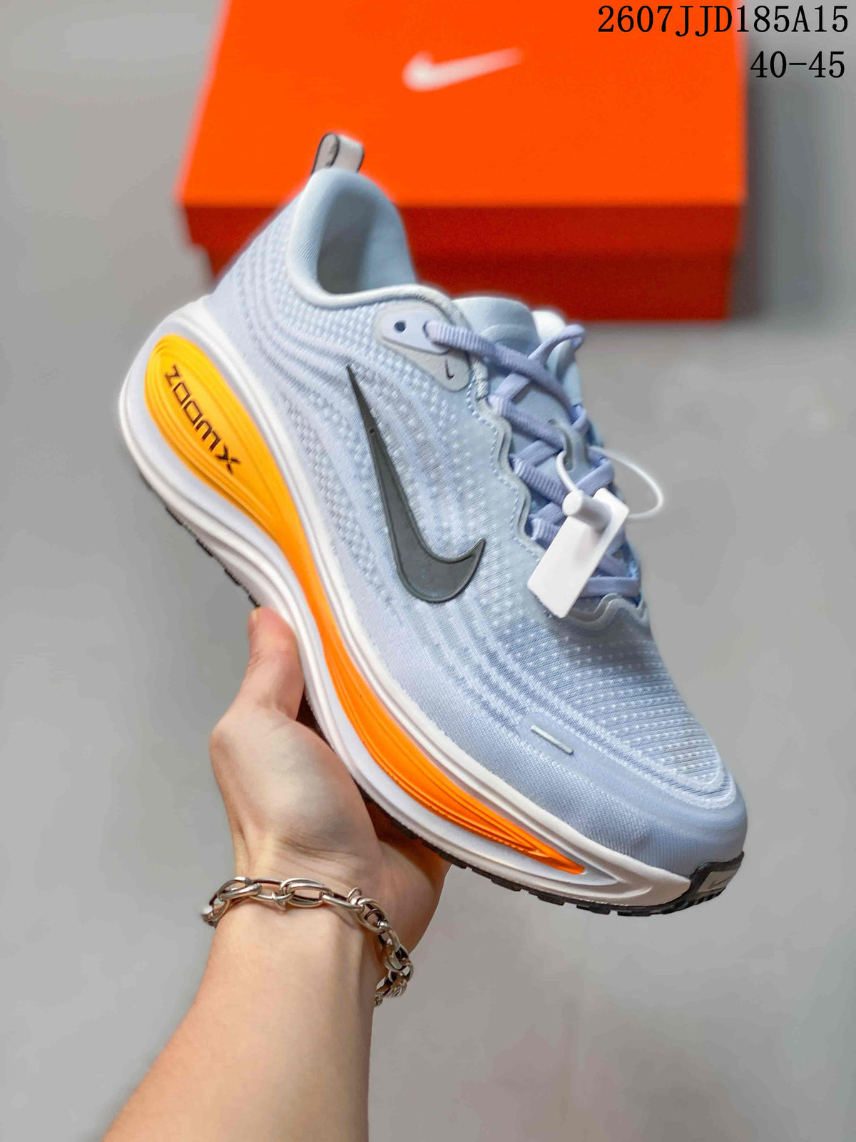 Angled side view of the light blue Nike Vomero Plus sneaker with orange midsole detailing and black outsole.