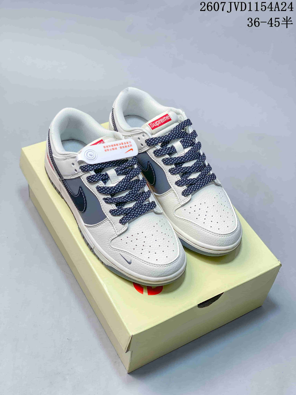 Pair of white, navy and gray Nike SB Dunk Low sneakers displayed on a branded shoe box.