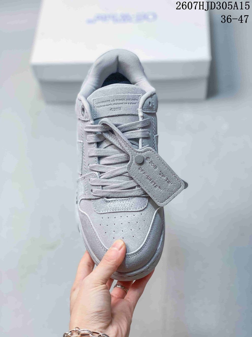 Top view of the gray sneaker showing flat laces, perforated toe box, tongue branding, and attached tag.