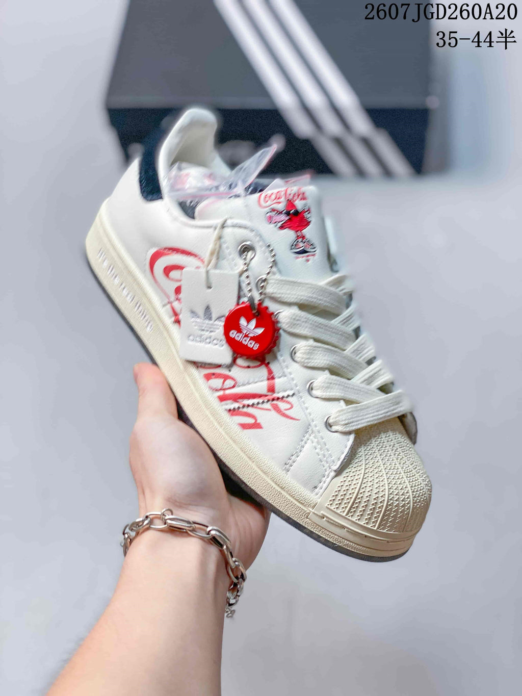 Angled side view showing Coca-Cola graphics, Adidas branding, decorative hangtags, and the shell toe.