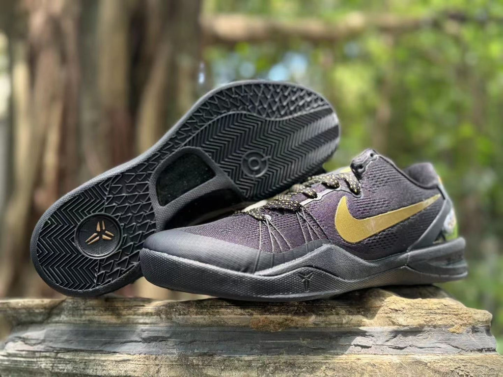 Black and gold sneaker pair displayed with one shoe lifted to show the patterned rubber outsole.