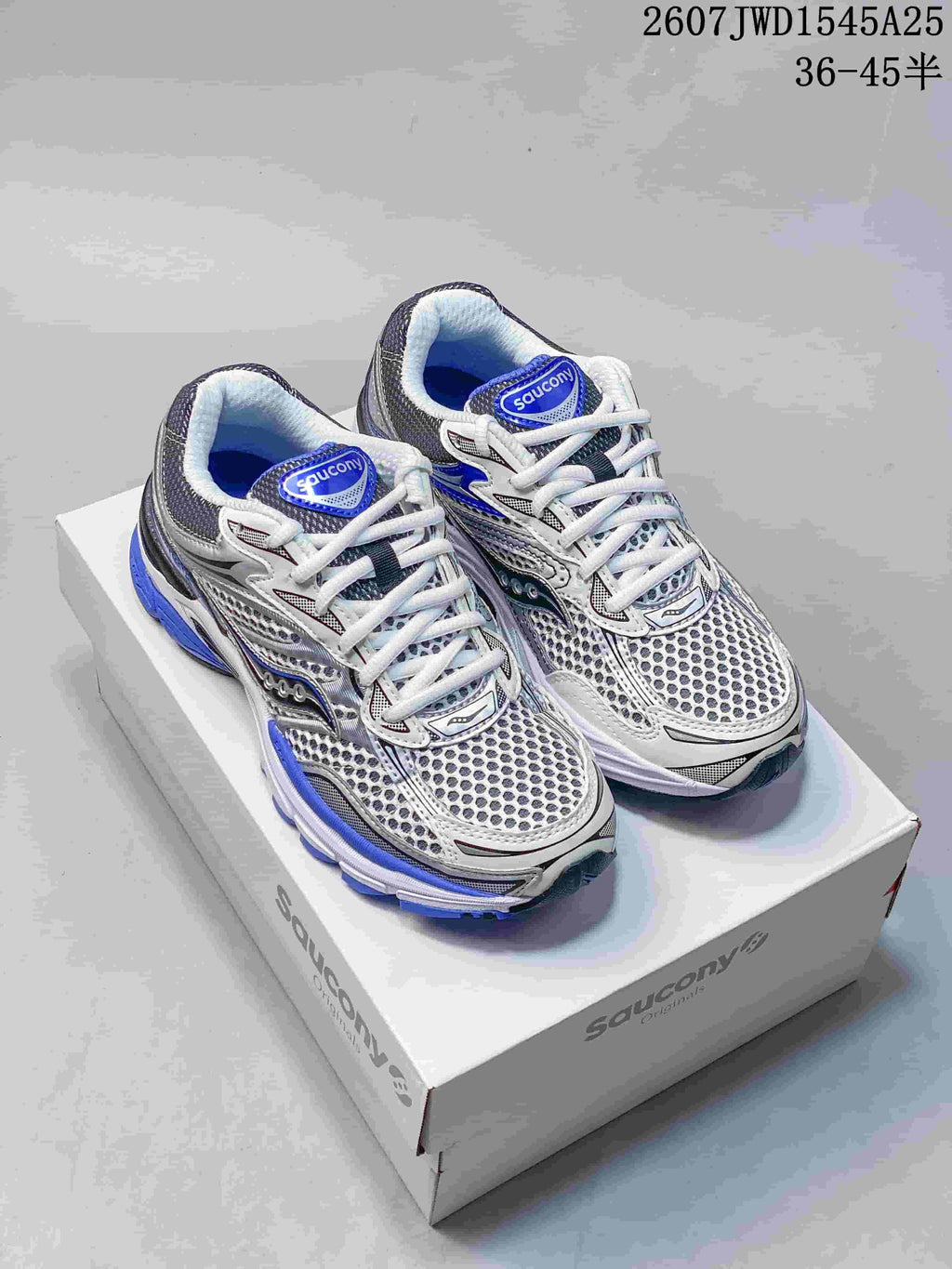 Pair of Saucony ProGrid Omni 9 sneakers on a shoebox, showing the white, gray and blue color scheme and source size text.