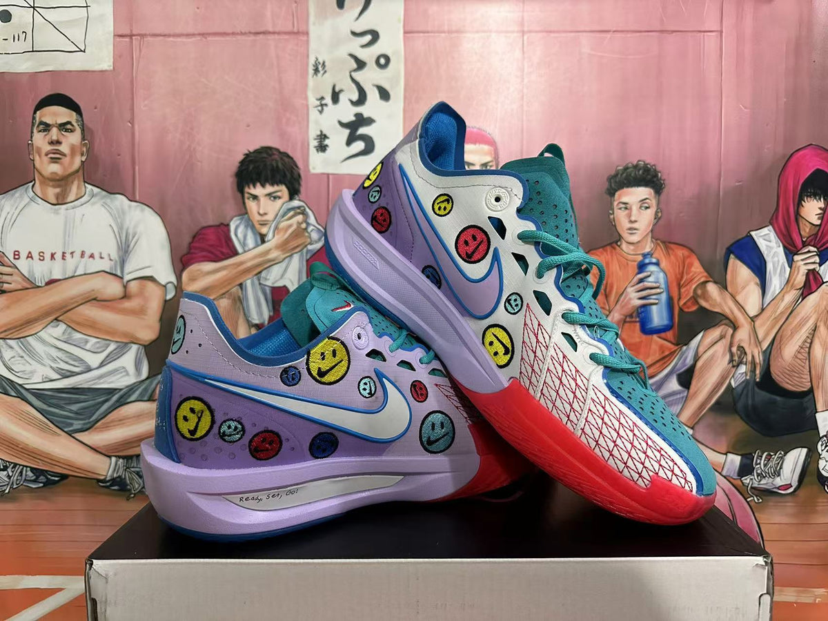 Angled view of the pair of Nike basketball sneakers, highlighting the colorful smiley-face graphics, Swoosh, and layered sole.