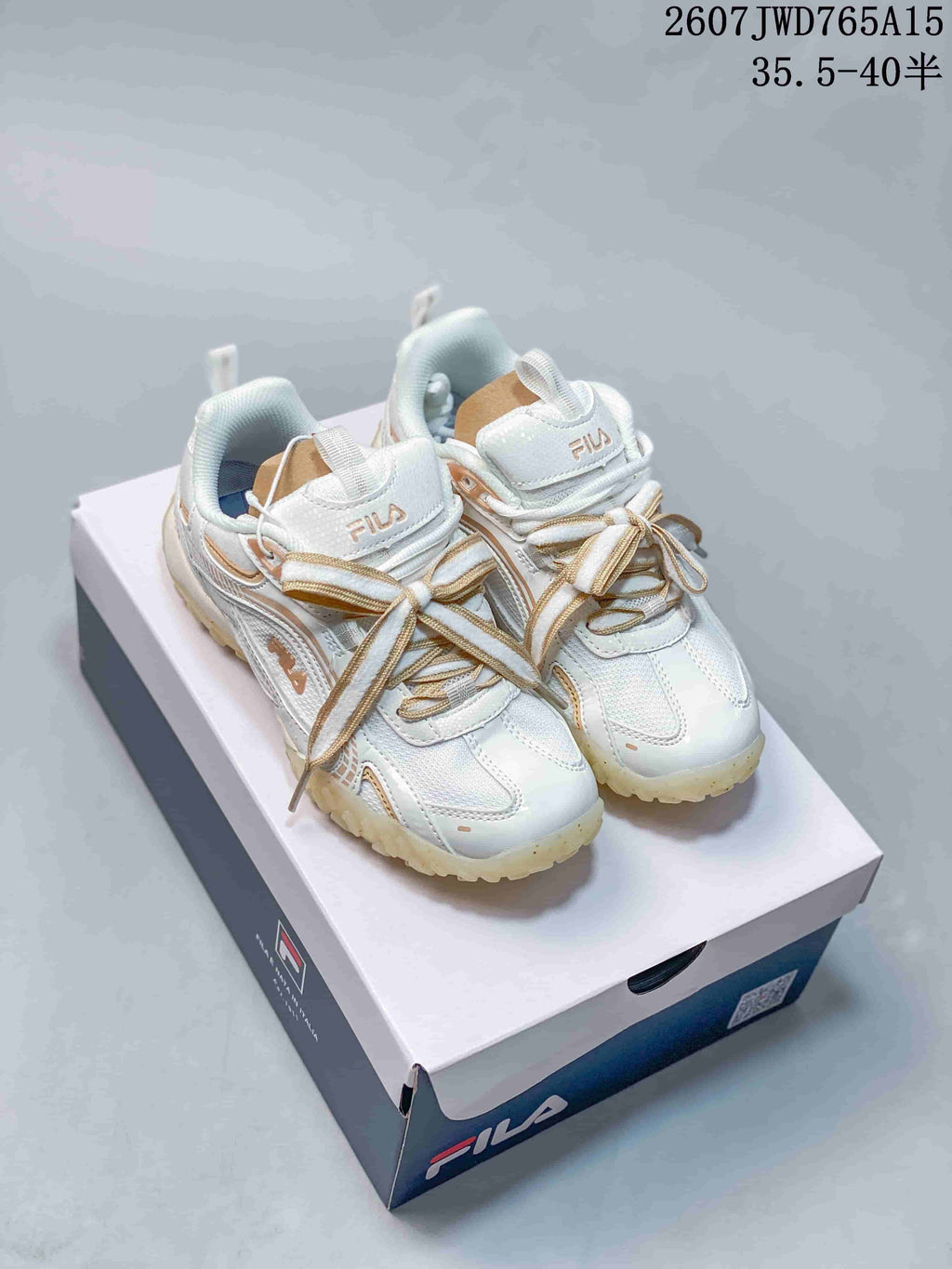 Pair of white and gold FILA Pebble sneakers displayed on a FILA shoebox, with the style reference and size range visible above.