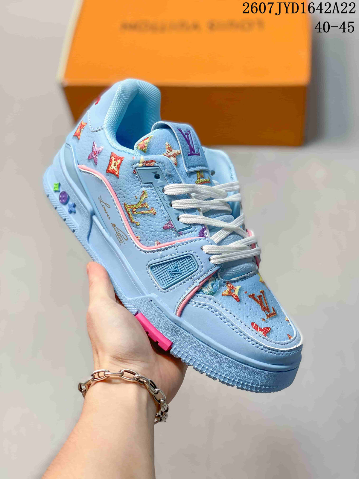 Angled side view of the light blue Louis Vuitton Trainer sneaker showing patterned panels, white laces, pink accents, and the low-top silhouette.