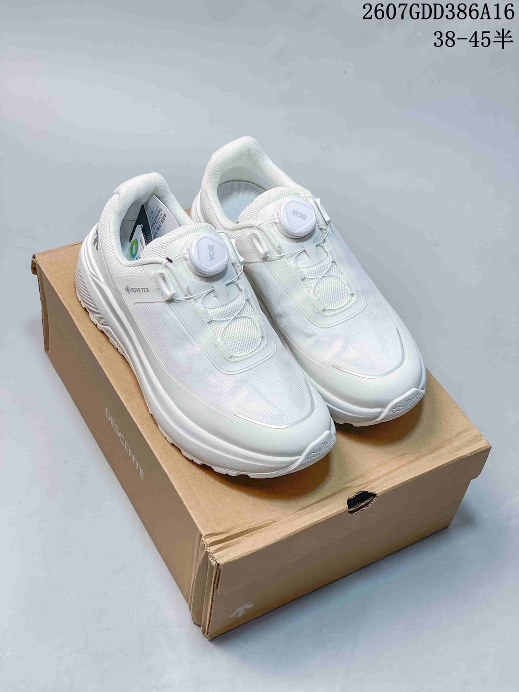 Pair of white DESCENTE low-top sneakers displayed on a cardboard shoebox, with product code and size-range text overlaid at the top.