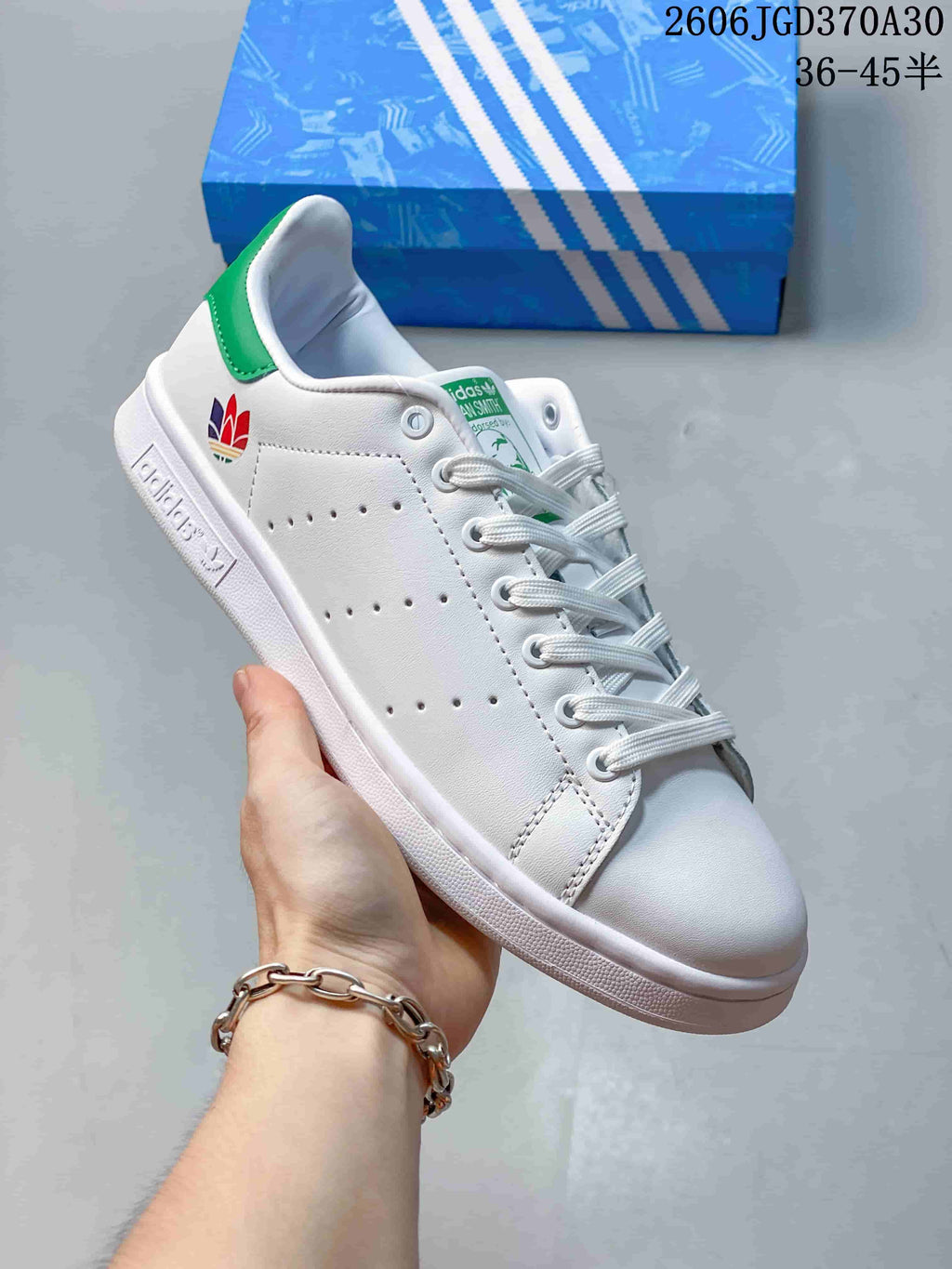 White Stan Smith-style sneaker with a multicolor heel emblem and a green heel tab.