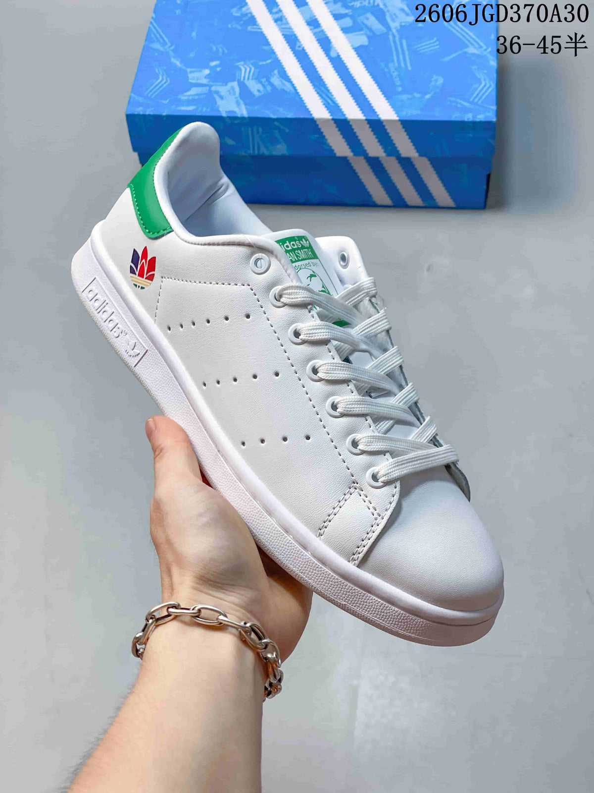 White Stan Smith-style sneaker with a multicolor heel emblem and a green heel tab.