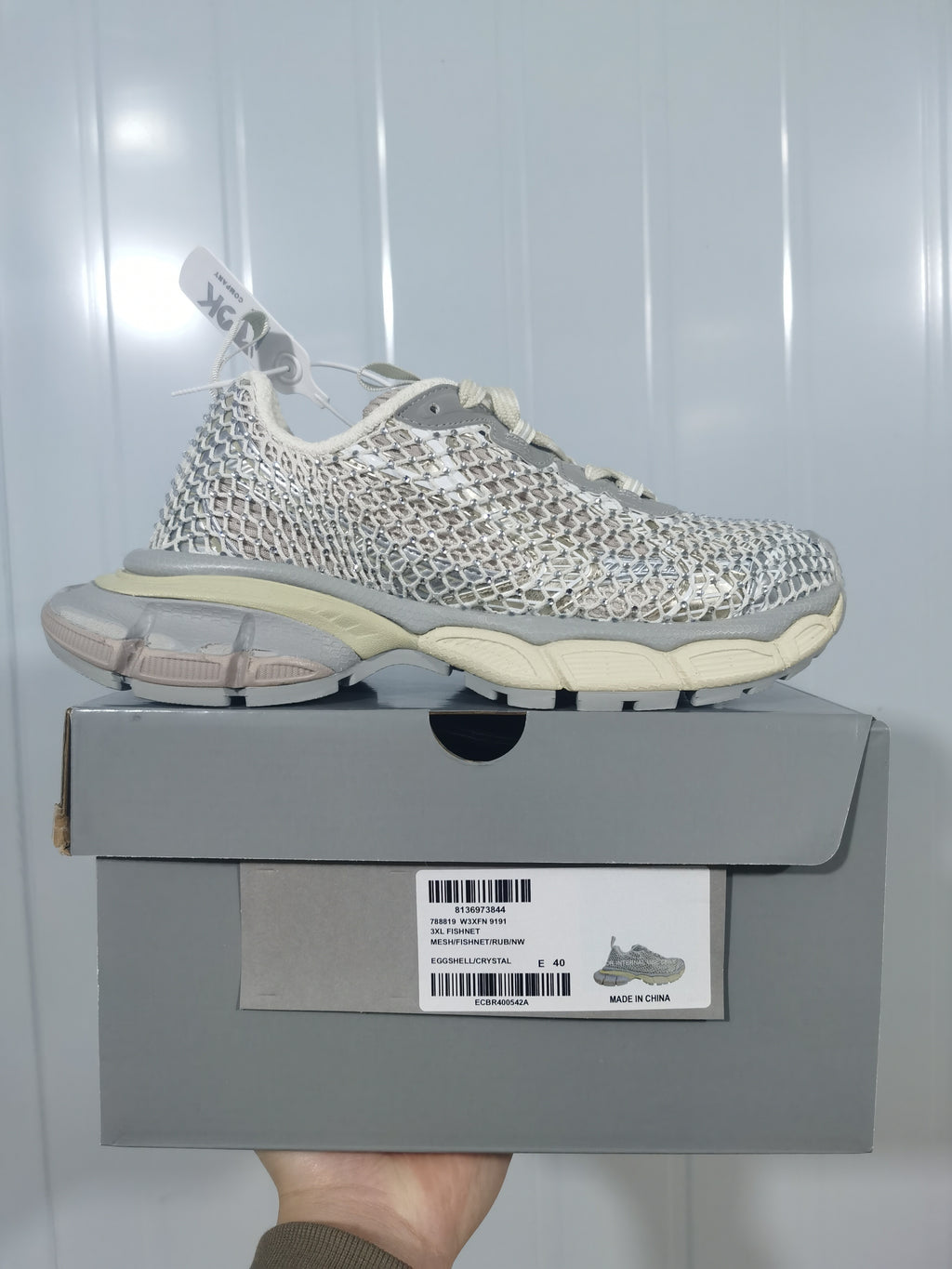 Side profile of the sneaker resting on its box; the box label shows color text including “EGGSHELL/CRYSTAL” and size EU 40.