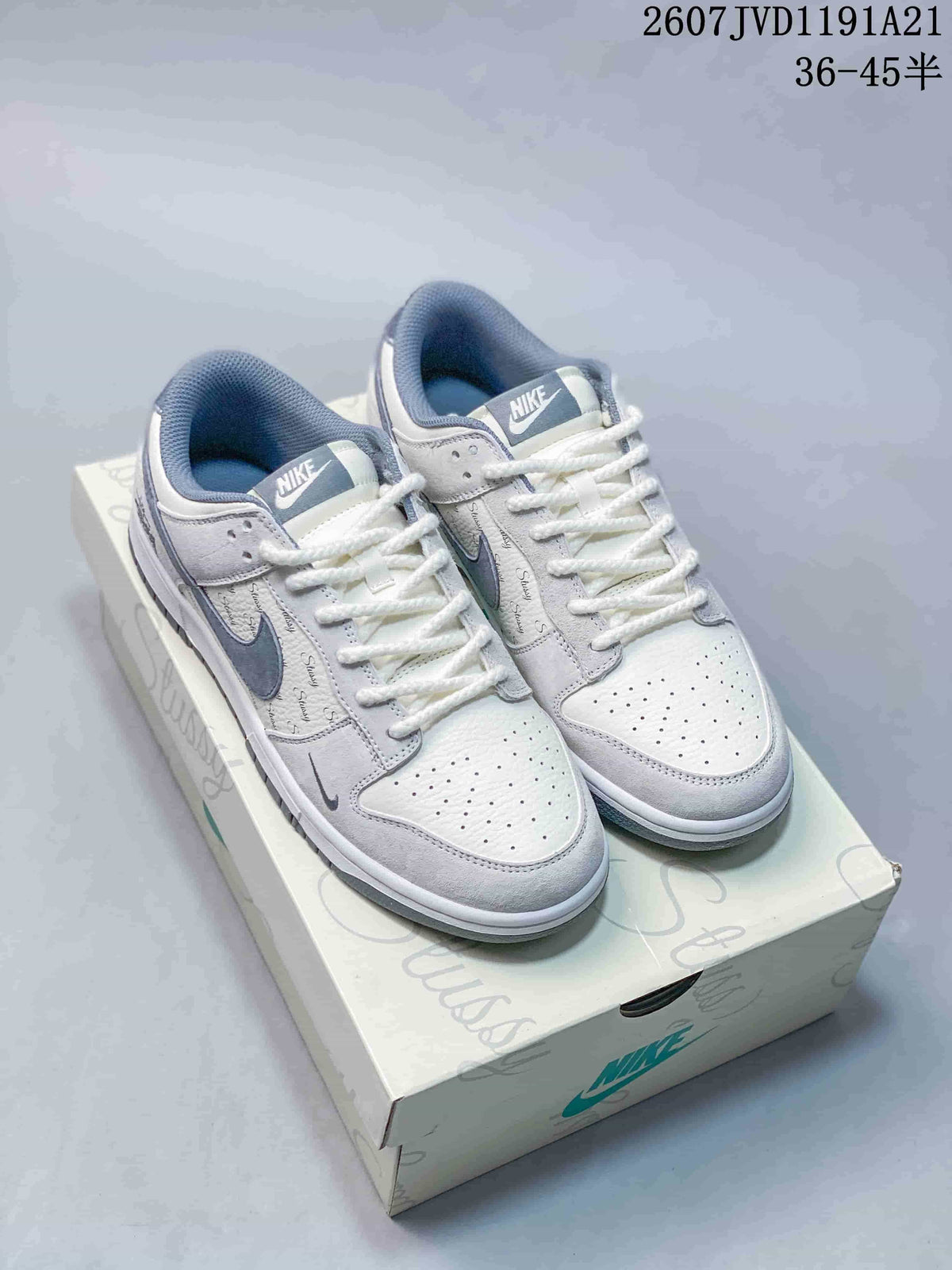 Pair of white and black Nike SB Dunk Low x Stussy sneakers shown on a branded shoe box; image text shows style code 2607JVD1191A21 and size range 36–45.