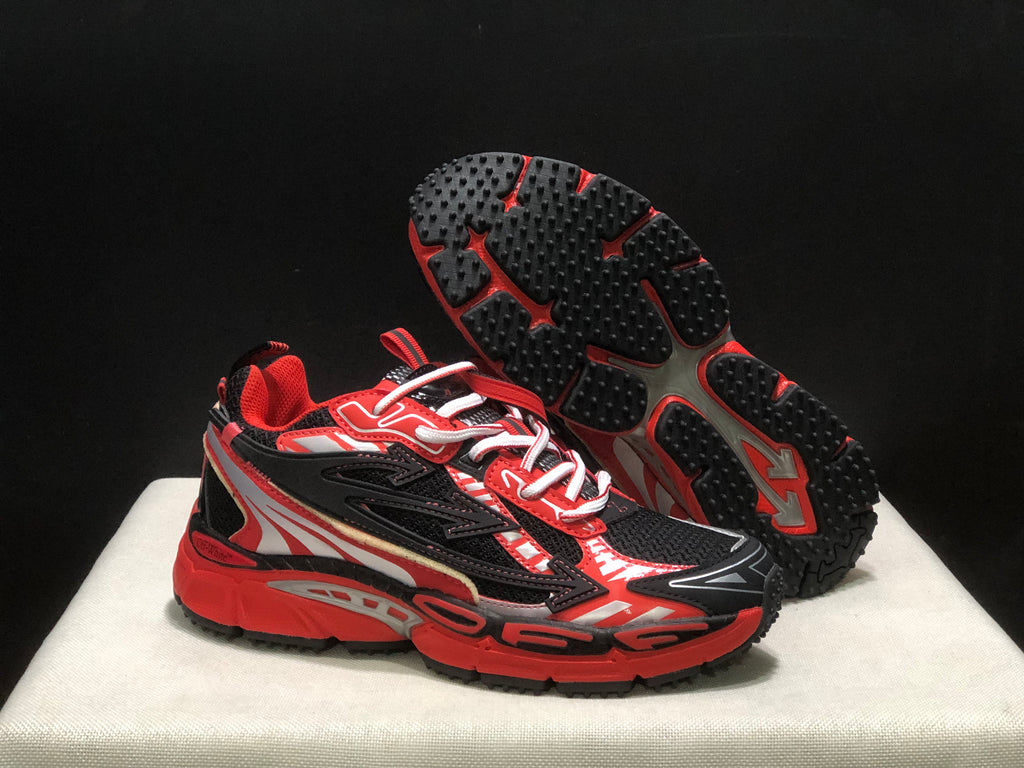Three-quarter view with one sneaker lifted to display the black textured outsole and red traction sections.
