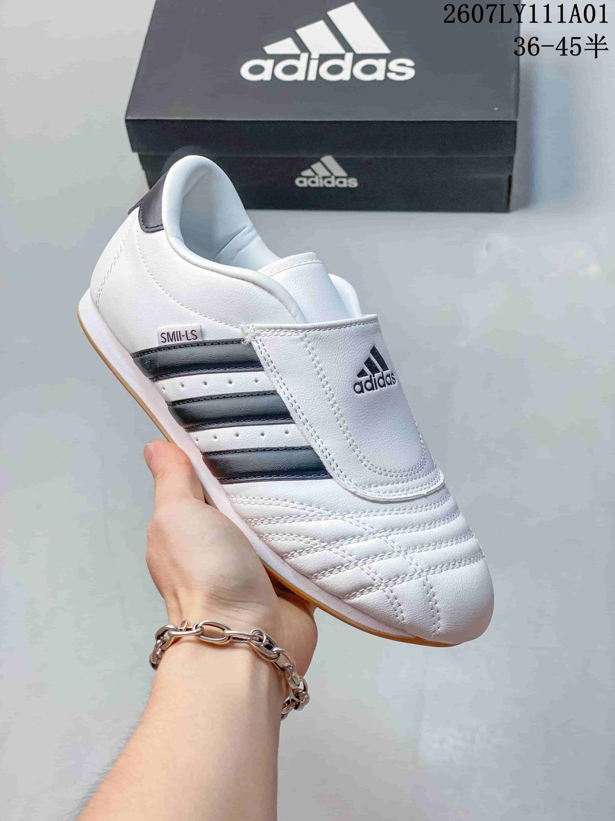 White Adidas Taekwondo low-top slip-on sneaker with dark stripes and a gum-colored outsole.