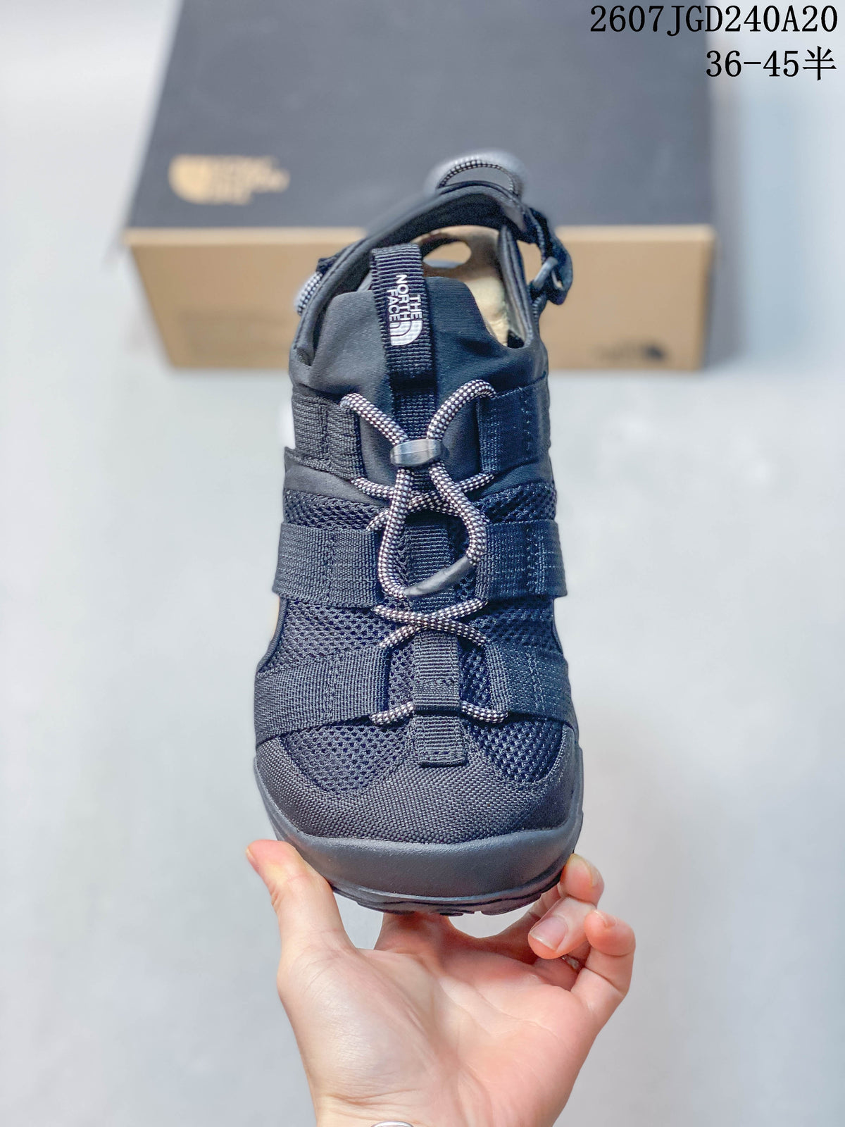 Front view of the sandal showing the open toe, layered straps, cord-style lacing, and dark mesh-like upper panels.