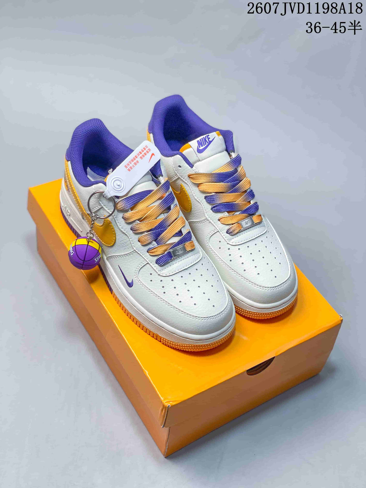 Pair of white Nike low-top sneakers with purple and gold details, displayed on an orange shoebox with a basketball accessory.