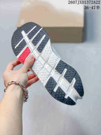 Underside view showing the sneakers' segmented outsole with dark textured rubber sections and red detailing.