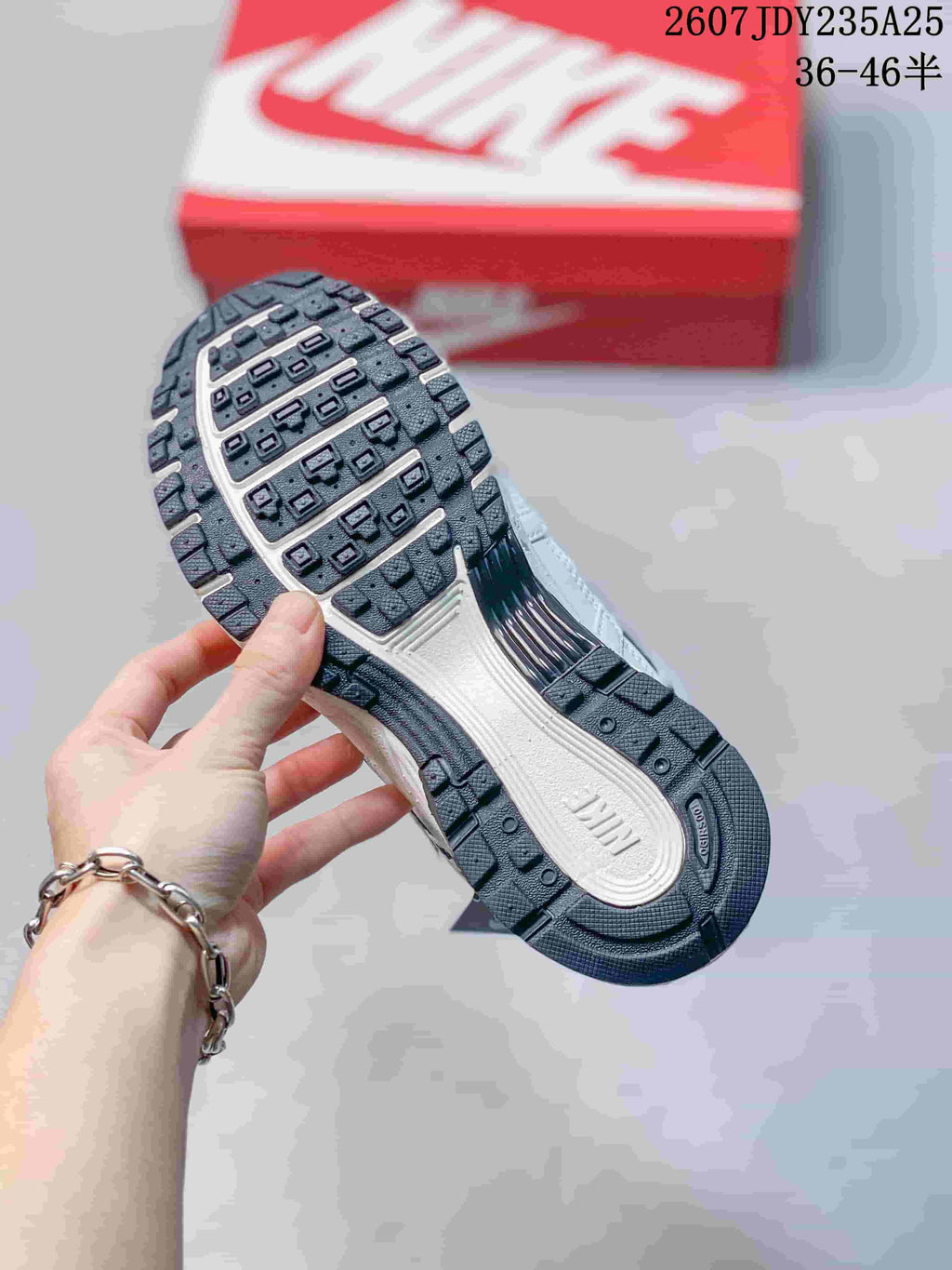 Close view of the patterned rubber outsole on a white and dark navy sneaker, with a red shoebox in the background.