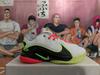 Side view of a grey and black Nike basketball shoe with lime green and coral accents