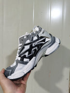 Side view of black, white, and gray Balenciaga Runner sneakers showing layered panels and a chunky sculpted sole.