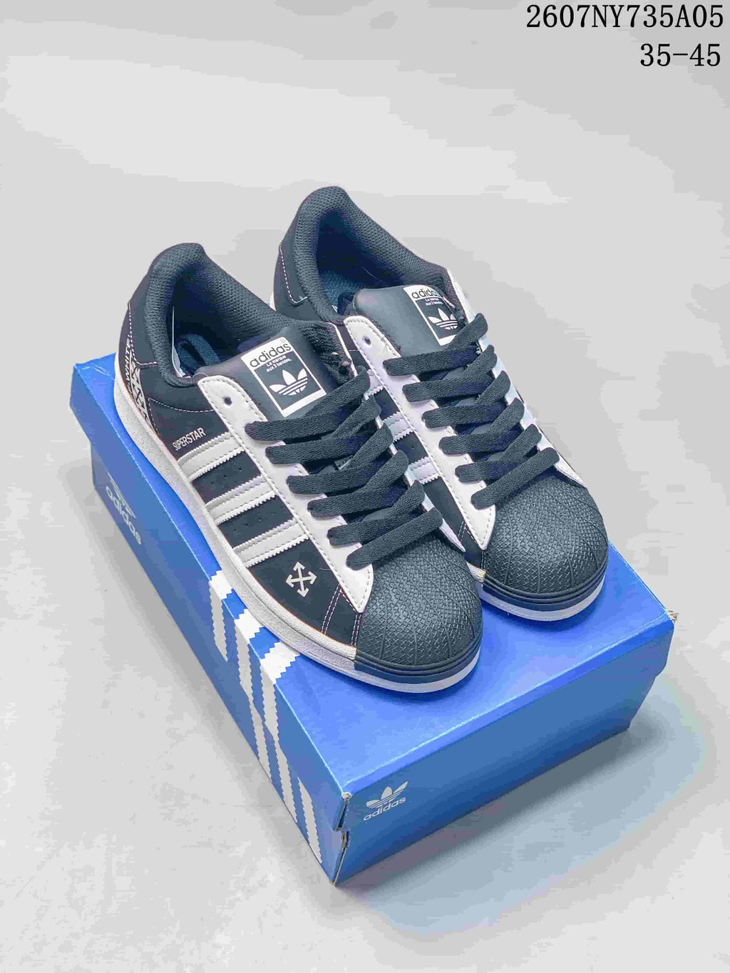 Pair of black and white Adidas Superstar sneakers displayed on a blue Adidas shoe box.