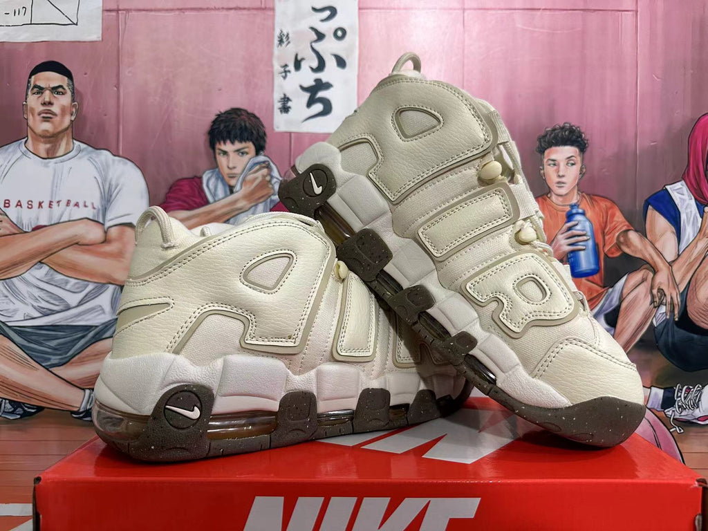 Pair of cream Nike Air More Uptempo sneakers displayed at an angle, showing AIR side lettering and dark outsole accents.