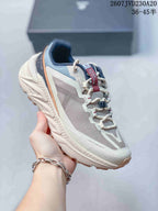 Three-quarter side view showing the off-white and gray upper, navy collar, orange trim, padded sole, and lugged outsole.