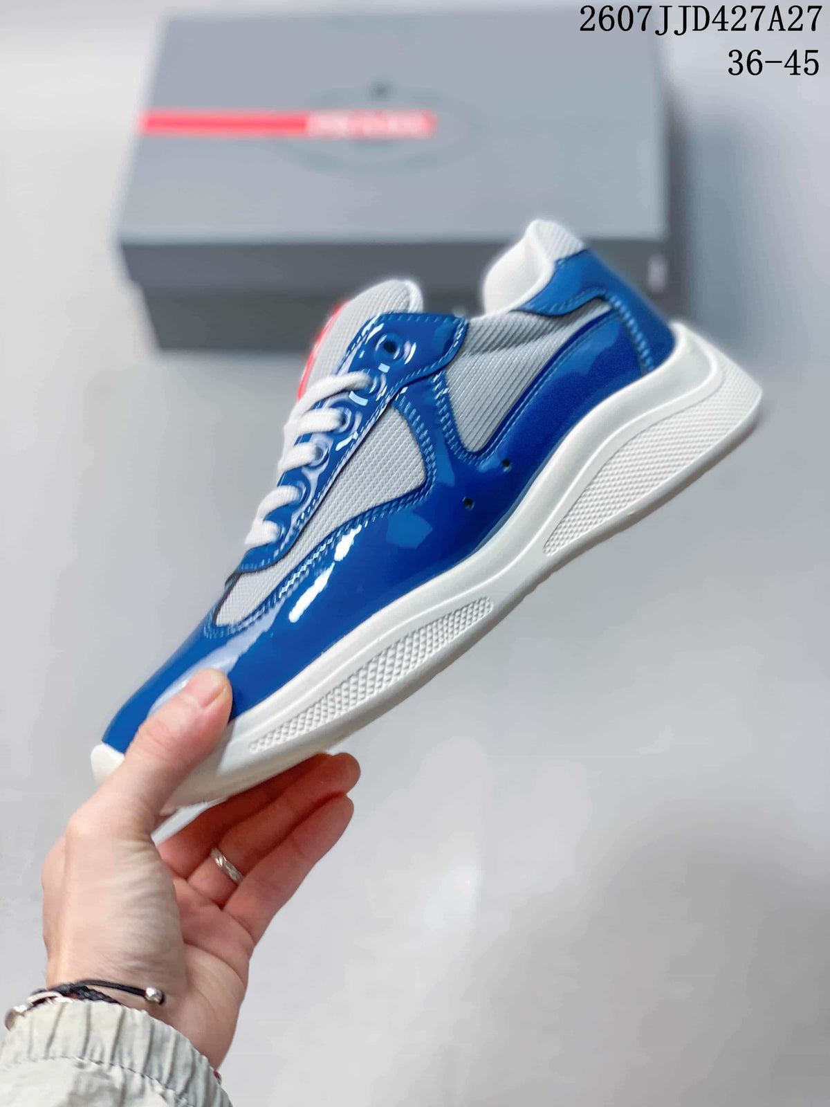 Side view of the sneaker showing glossy blue panels, gray mesh-style sections, white laces, and a white sole.