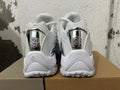 Rear view of white Nike NOCTA Glide sneakers with reflective silver-tone heel details.