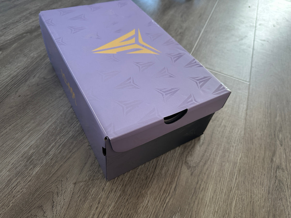 Angled view of a light purple shoe box with a gold-colored logo