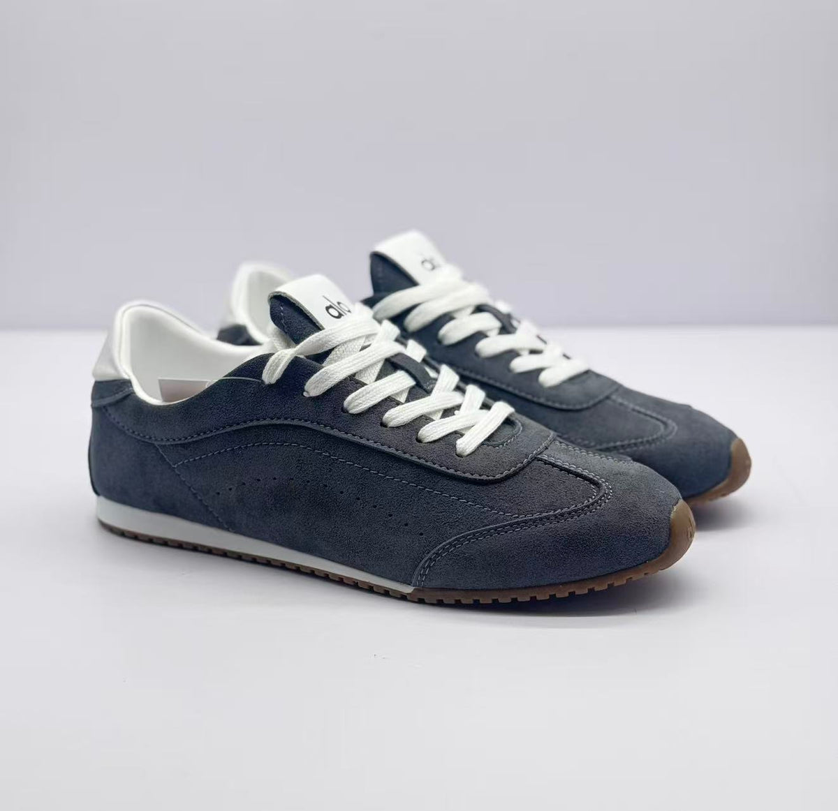 Three-quarter front view of the carbon gray Alo sneakers with white laces and contrasting collars.