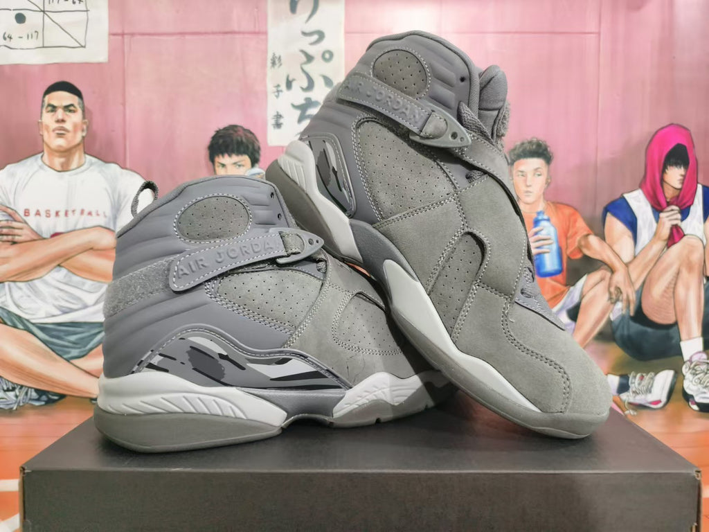 Pair of grey Jordan high-top sneakers displayed at an angle, showing the side panels and cross-strap design.