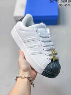 Angled side view of the white sneaker with layered three-stripe panels, black shell toe, and white rubber sole.
