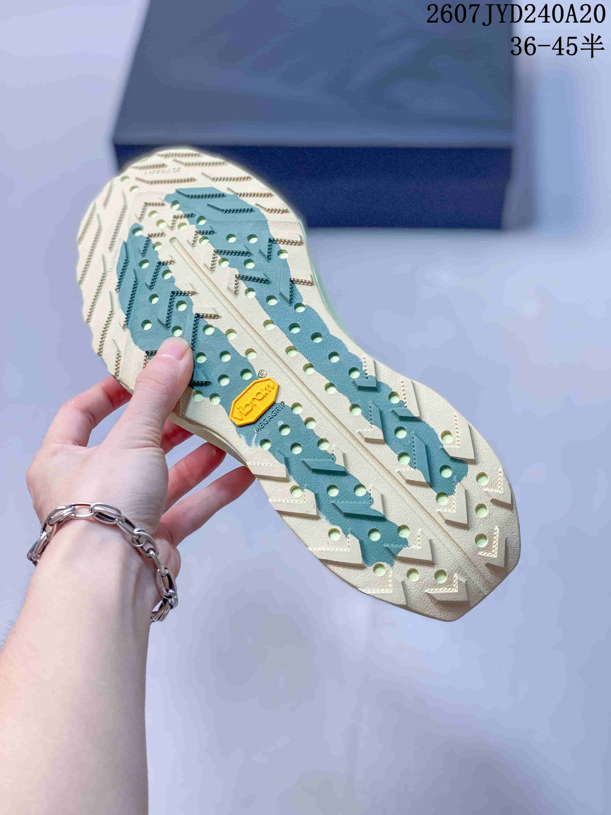 Close view of the sneaker outsole showing a pale rubber base, green sections, perforations, and a lugged tread pattern.