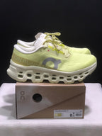 Side view of a light yellow On Cloudmonster 3 sneaker with a sculpted white midsole and product box.